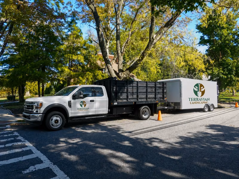 A Terravian Landscaping crew truck with its equipment trailer, parked on a tree-lined street
