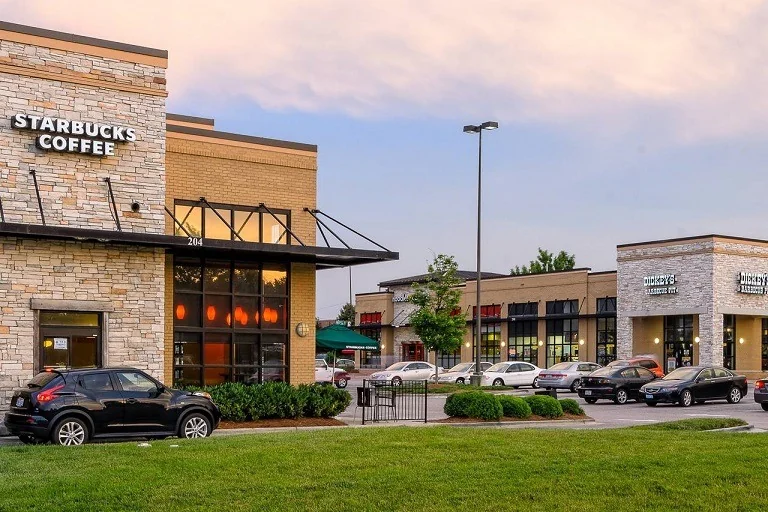 A retail center with a clean lawn edge, trimmed beds, and a full parking lot